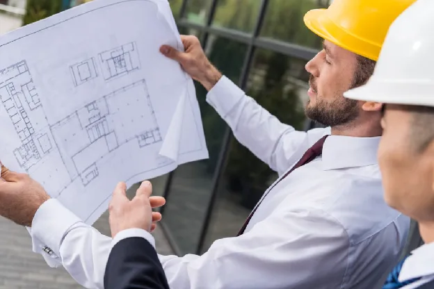 Two construction professionals in hard hats reviewing architectural blueprints on a job site